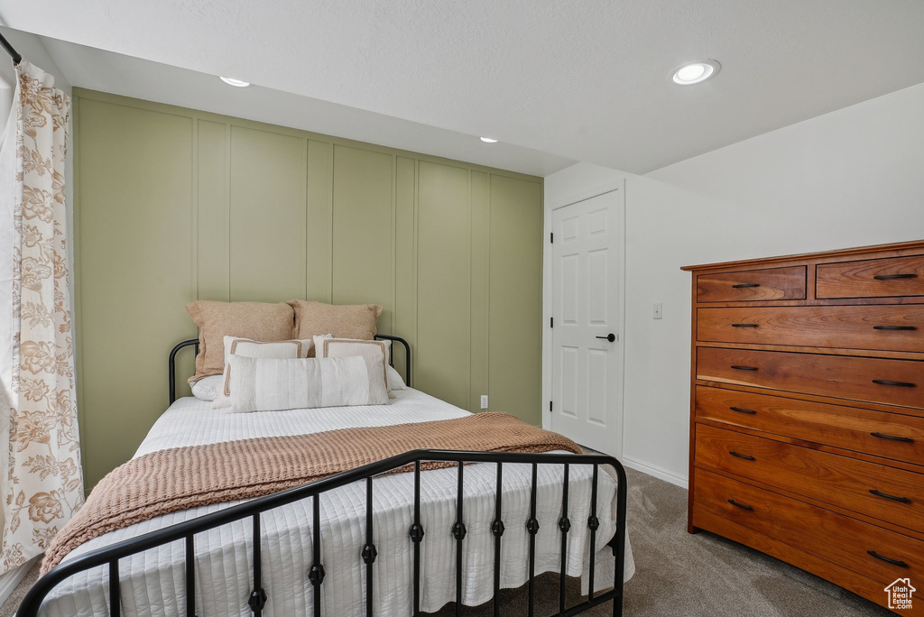 Bedroom with dark colored carpet, recessed lighting, and a decorative wall