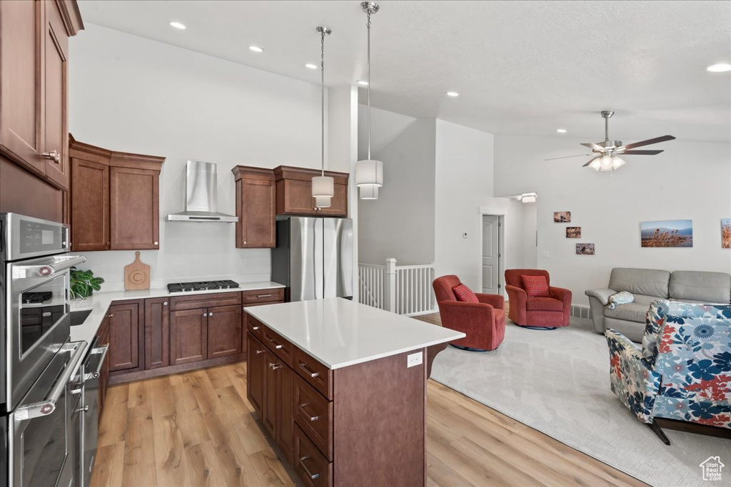 Kitchen featuring wall chimney range hood, open floor plan, appliances with stainless steel finishes, and light wood-style floors