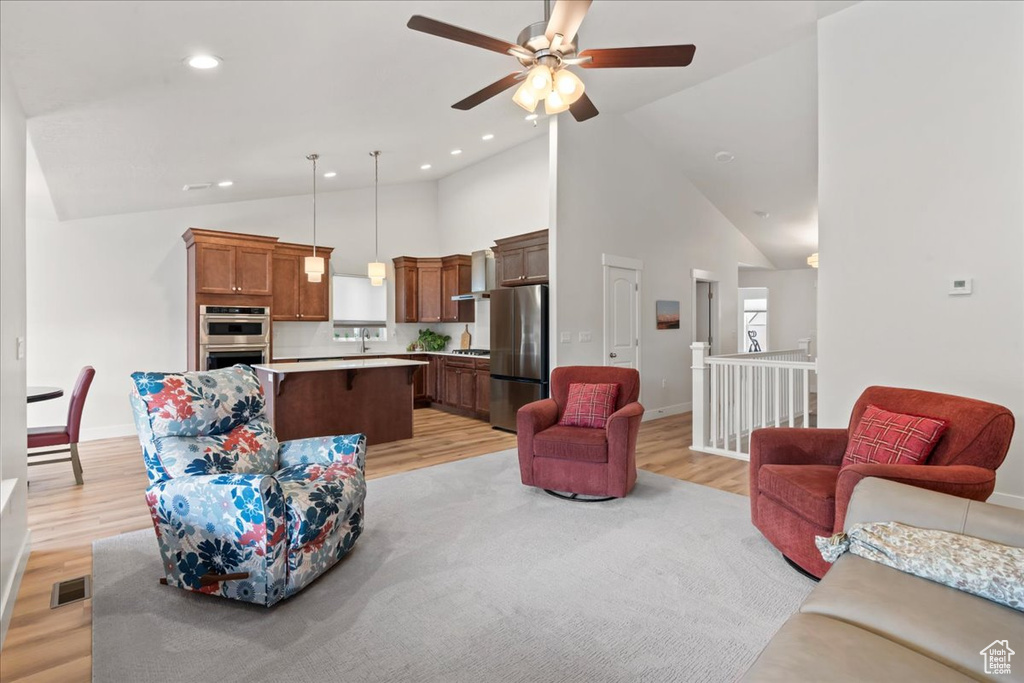 Living area with high vaulted ceiling, light wood-style flooring, a ceiling fan, baseboards, and visible vents