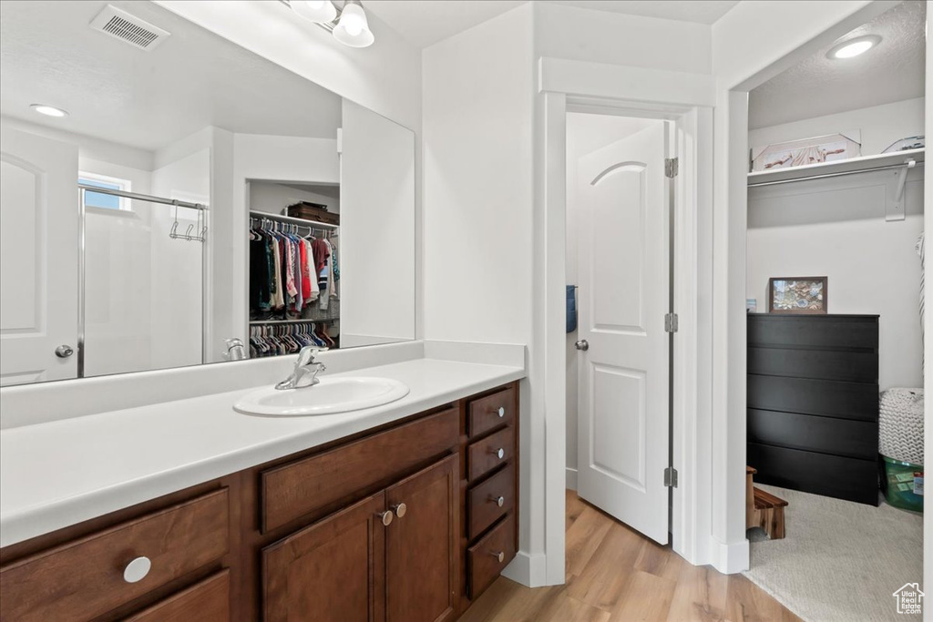 Full bathroom with a walk in closet, vanity, wood finished floors, an enclosed shower, and visible vents