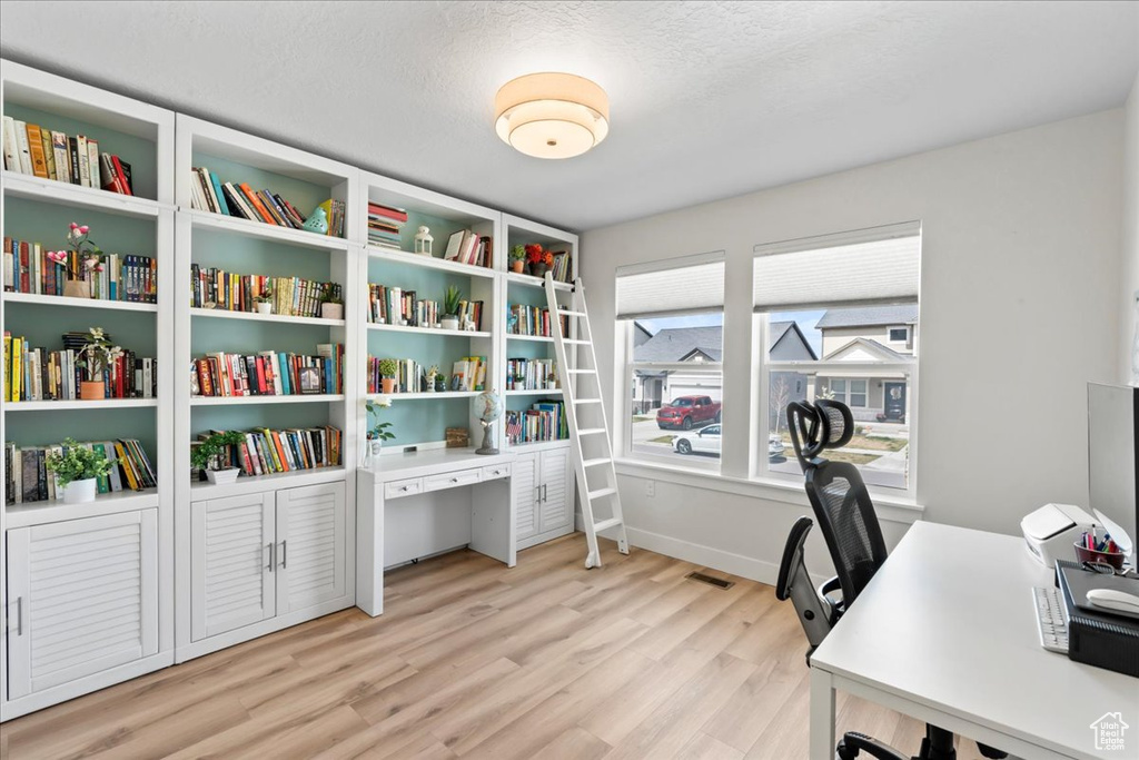Office space featuring a textured ceiling, visible vents, baseboards, and light wood-type flooring