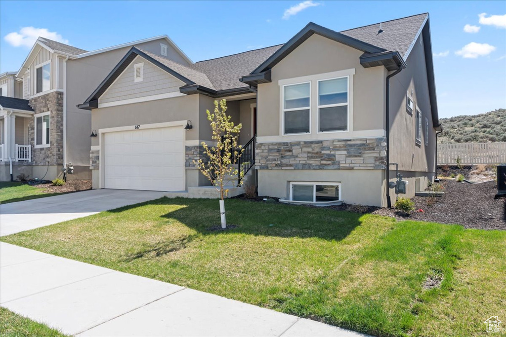 View of front of property with driveway, a front yard, an attached garage, stone siding, and stucco siding