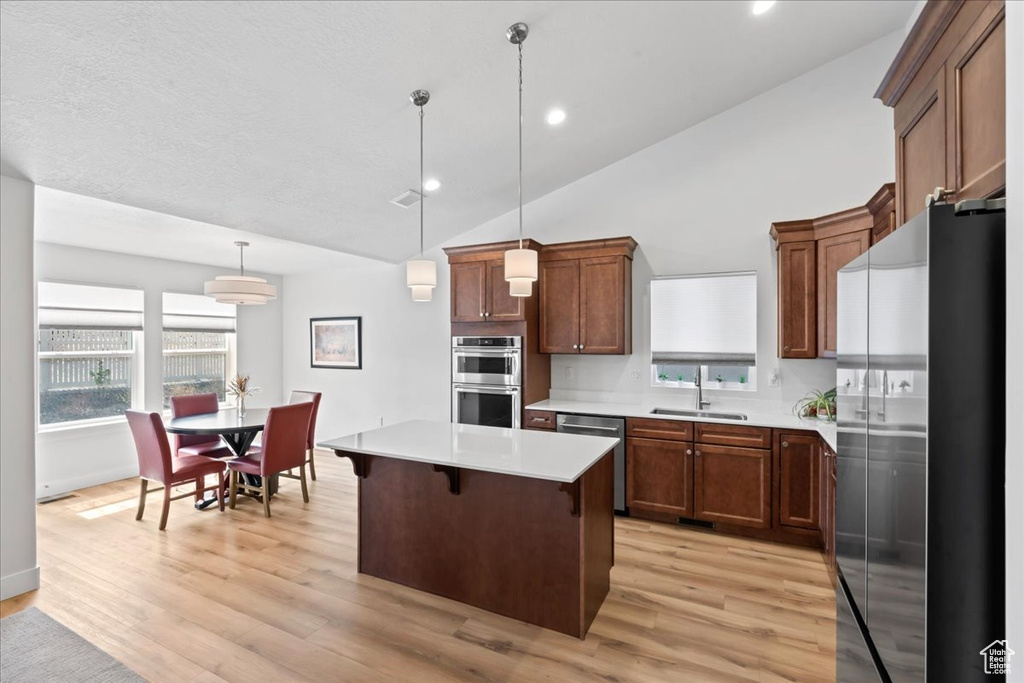 Kitchen featuring light countertops, a sink, lofted ceiling, stainless steel appliances, and light wood-style flooring