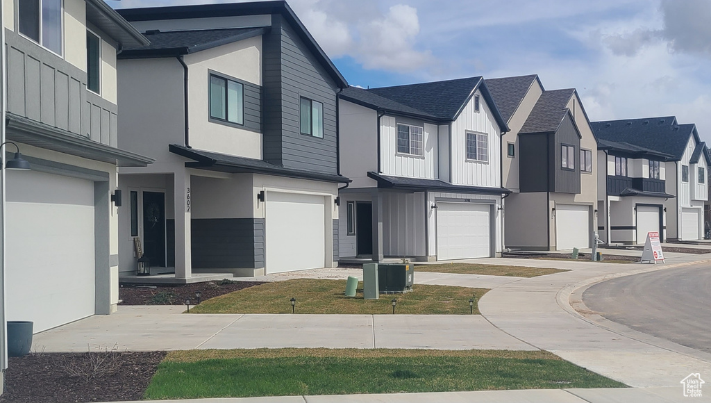 View of front facade featuring driveway, a residential view, an attached garage, a shingled roof, and stucco siding