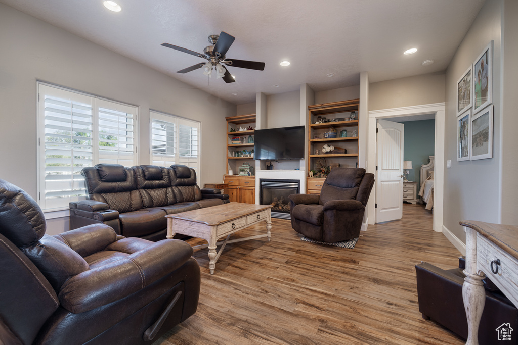 Living area with a glass covered fireplace, a ceiling fan, recessed lighting, and wood finished floors