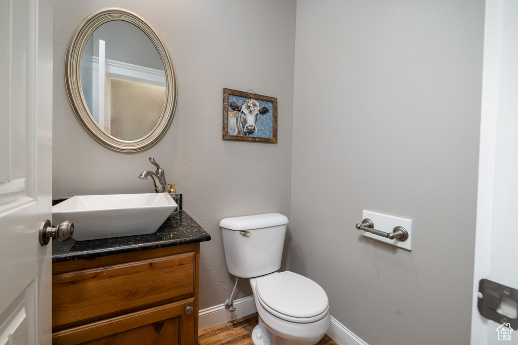 Half bathroom featuring vanity, baseboards, wood finished floors, and toilet