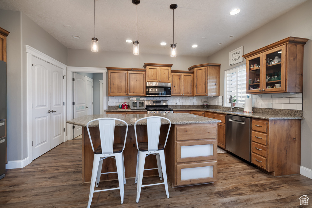 Kitchen with decorative backsplash, brown cabinetry, a kitchen island, appliances with stainless steel finishes, and a sink