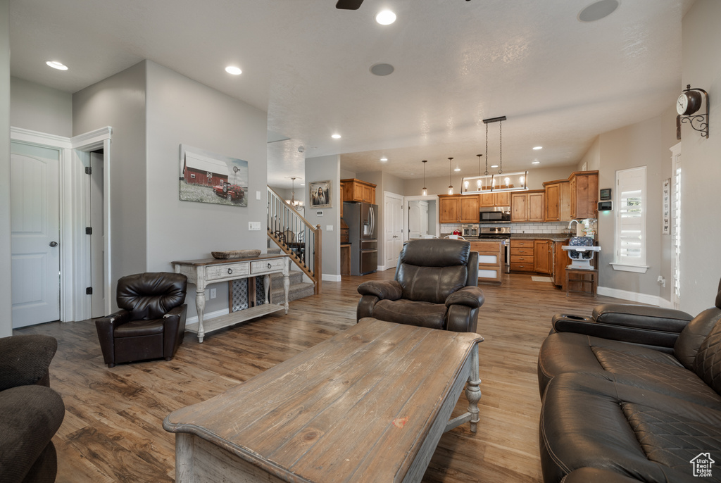 Living area featuring light wood-style floors, ceiling fan with notable chandelier, stairs, recessed lighting, and baseboards