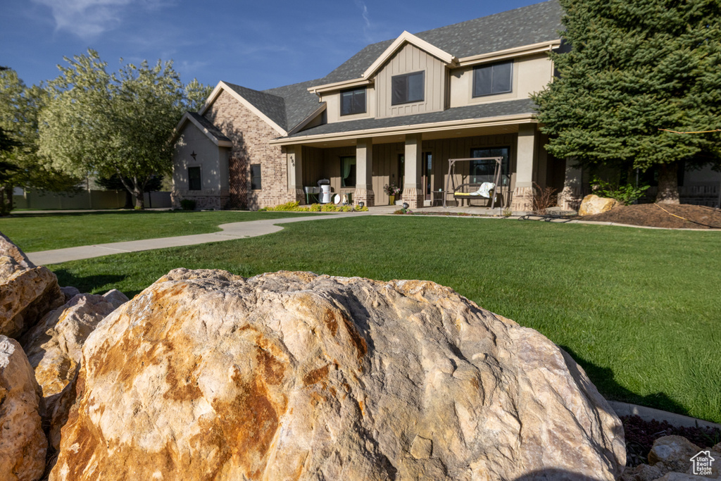 Craftsman-style home featuring board and batten siding, covered porch, stone siding, and a front lawn
