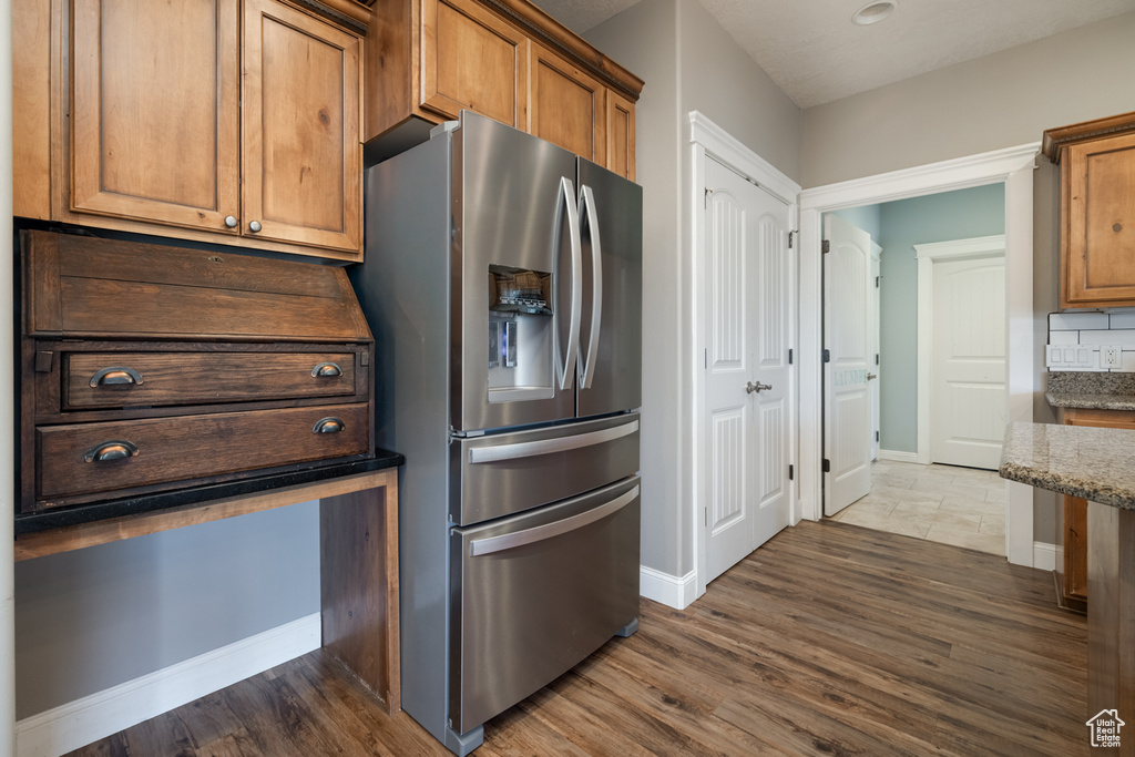 Kitchen featuring dark wood-style flooring, stone countertops, brown cabinetry, and stainless steel fridge with ice dispenser