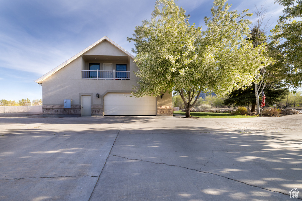 View of front of house featuring driveway, fence, a balcony, an attached garage, and stucco siding