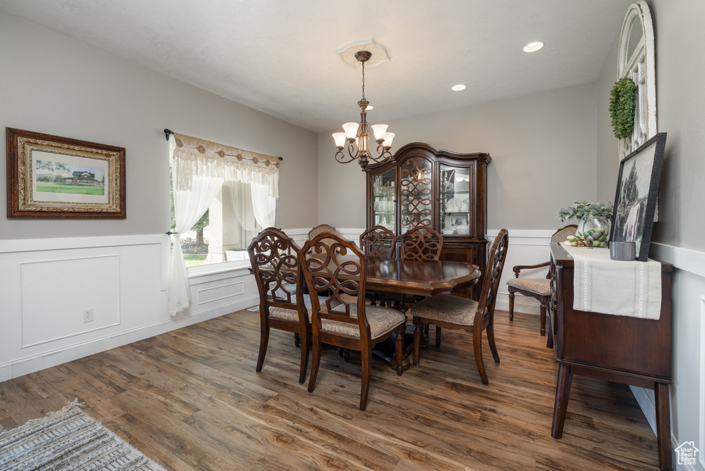 Dining room with a decorative wall, wood finished floors, a chandelier, and a wainscoted wall