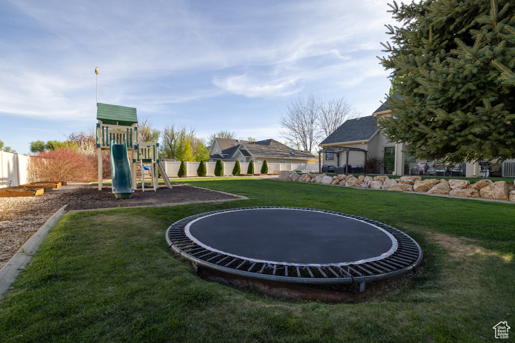 View of yard with a playground, fence, and a trampoline