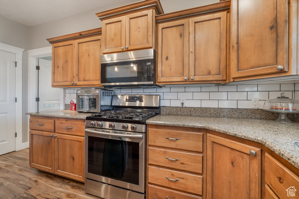 Kitchen with backsplash, brown cabinets, appliances with stainless steel finishes, and light wood-type flooring
