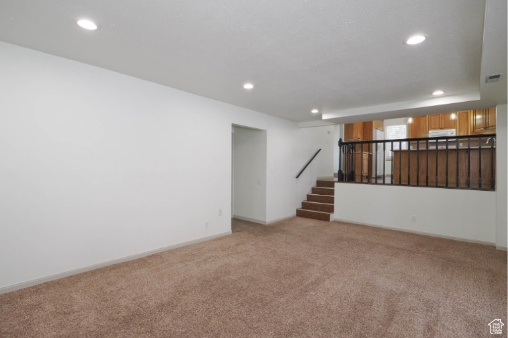 Unfurnished living room featuring visible vents, light carpet, baseboards, stairway, and recessed lighting