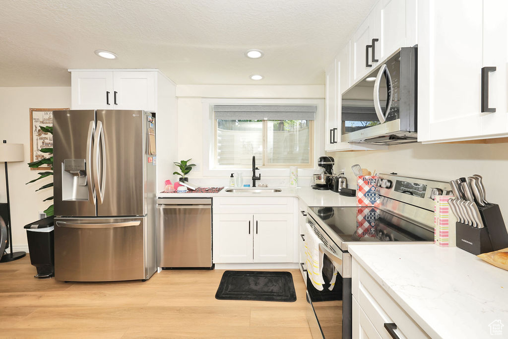 Kitchen featuring appliances with stainless steel finishes, white cabinetry, a sink, recessed lighting, and light wood-style flooring