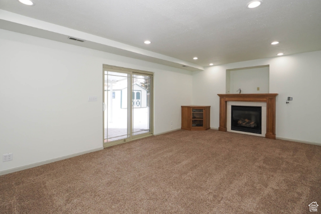 Unfurnished living room with recessed lighting, carpet flooring, baseboards, and a glass covered fireplace