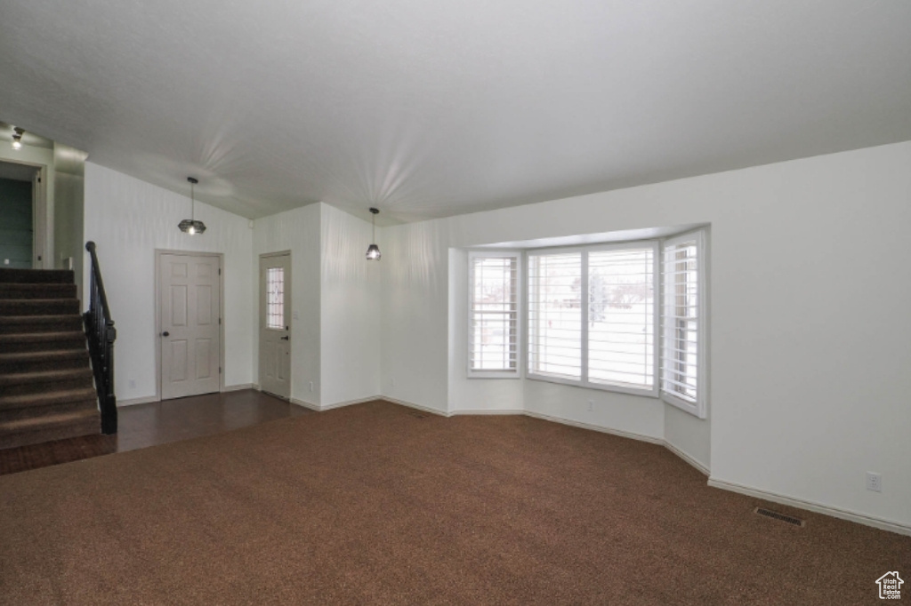 Unfurnished living room featuring visible vents, vaulted ceiling, baseboards, dark colored carpet, and stairs