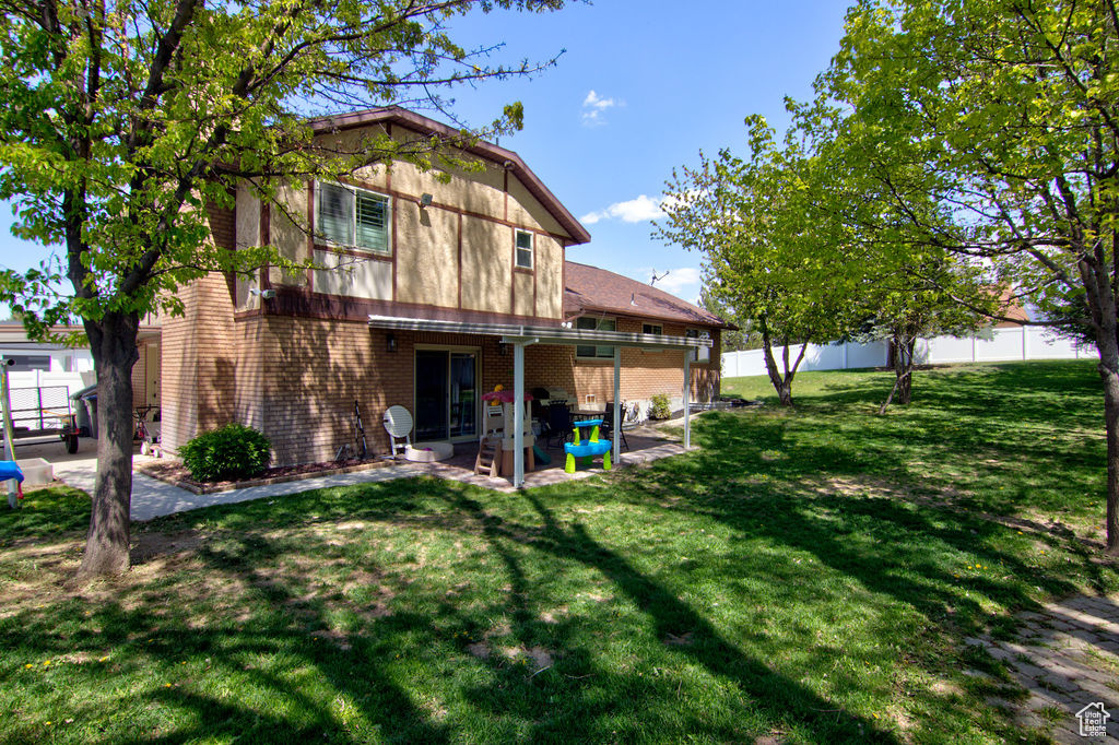 Back of house with brick siding, a fenced backyard, a lawn, and a patio area