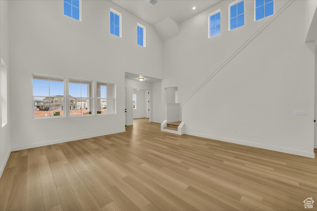 Unfurnished living room featuring light wood-type flooring, baseboards, and a towering ceiling