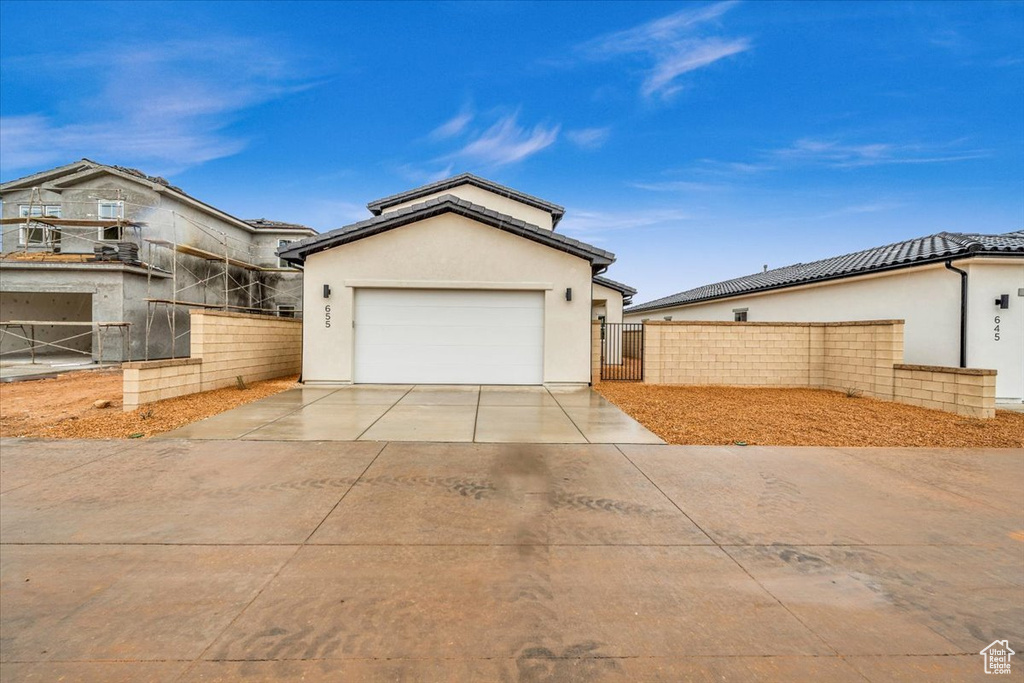 View of front of property featuring a gate, a garage, fence, concrete driveway, and stucco siding