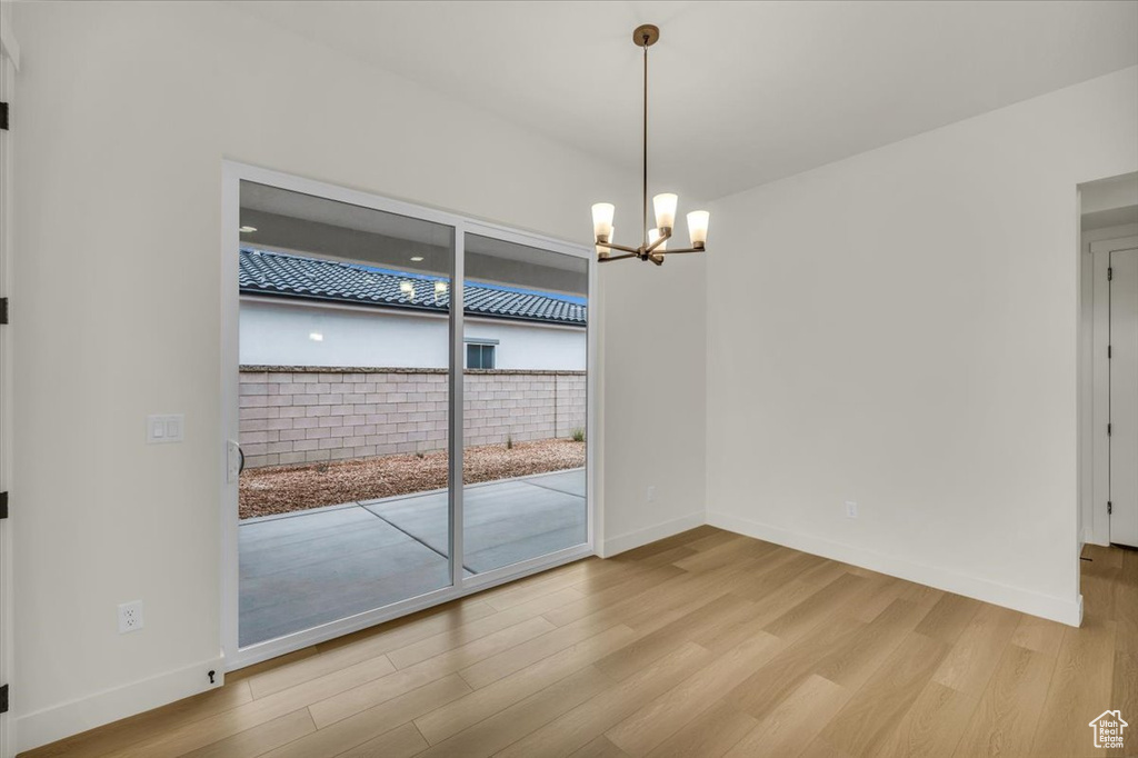 Unfurnished room with light wood-type flooring, baseboards, and a notable chandelier