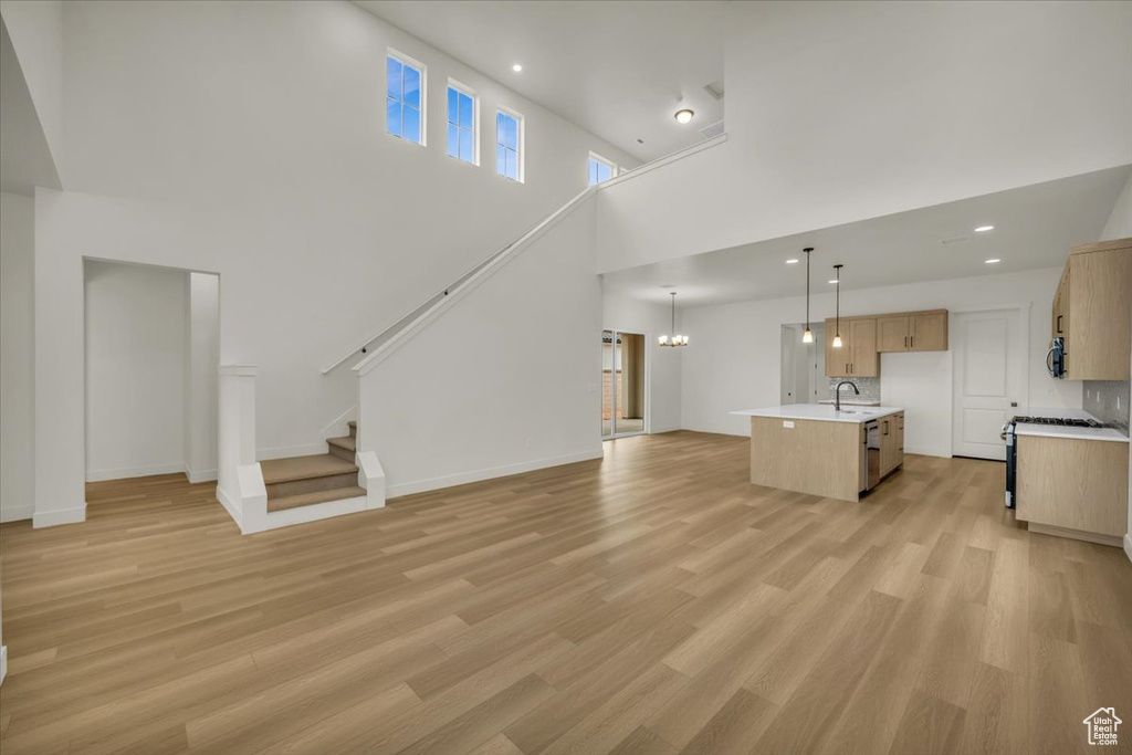 Unfurnished living room featuring a high ceiling, a notable chandelier, a sink, and light wood-type flooring