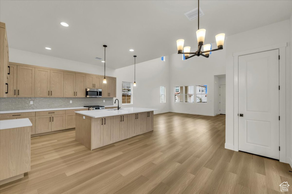 Kitchen with light brown cabinetry, an inviting chandelier, light countertops, stainless steel microwave, and light wood-type flooring