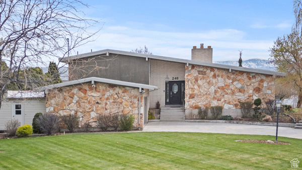 View of front of home with a chimney, a front yard, and stone siding
