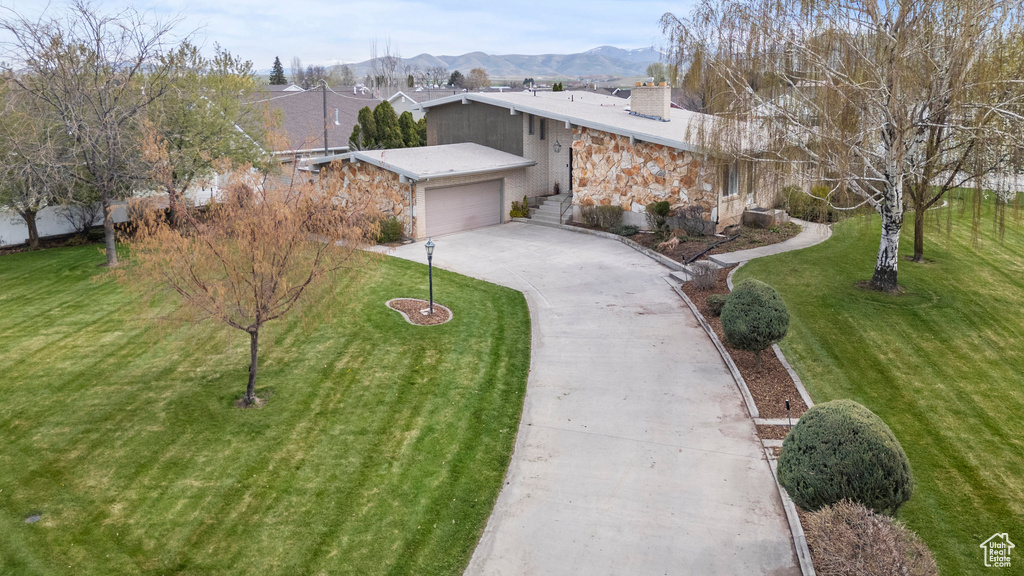 View of front of property featuring stone siding, a garage, a front yard, a chimney, and driveway