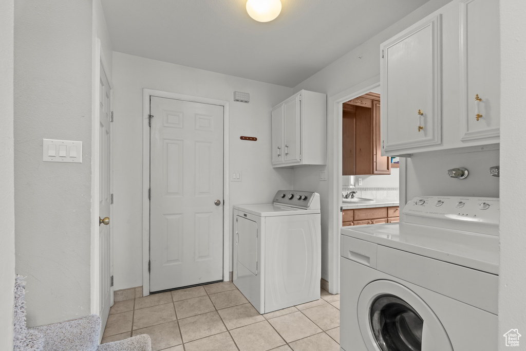 Washroom featuring a sink, light tile patterned flooring, cabinet space, and washing machine and clothes dryer