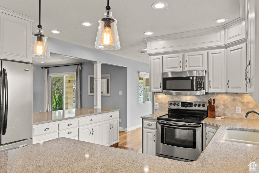 Kitchen with hanging light fixtures, a sink, stainless steel appliances, backsplash, and ornate columns