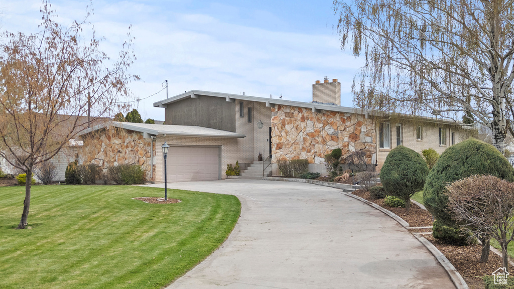 Mid-century inspired home featuring a front lawn, stone siding, a garage, a chimney, and driveway