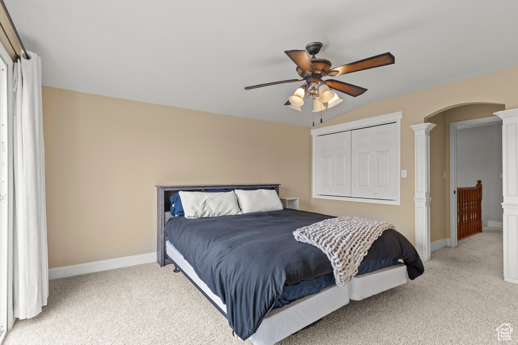 Bedroom with decorative columns, lofted ceiling, light carpet, baseboards, and arched walkways
