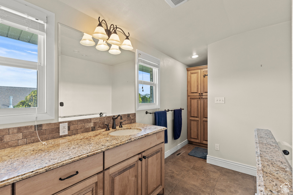 Bathroom featuring baseboards, a notable chandelier, decorative backsplash, and vanity