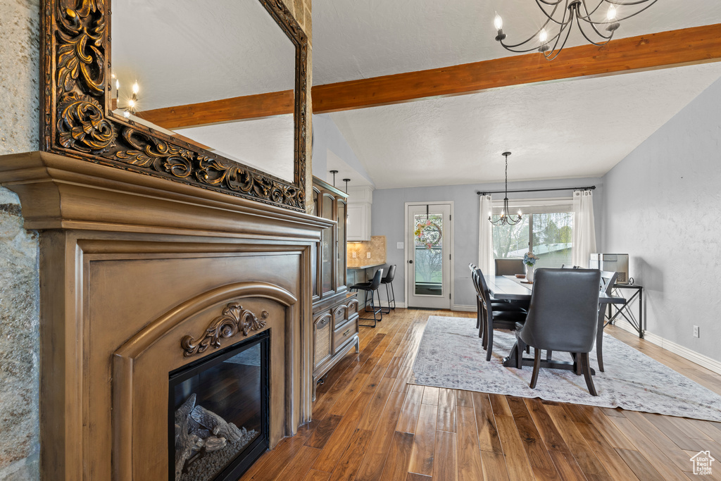 Dining area featuring dark wood-style flooring, an inviting chandelier, a glass covered fireplace, and vaulted ceiling with beams