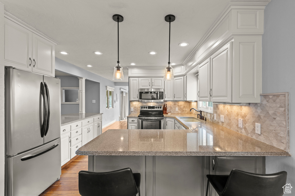 Kitchen featuring a sink, white cabinets, a peninsula, stainless steel appliances, and light wood-style flooring