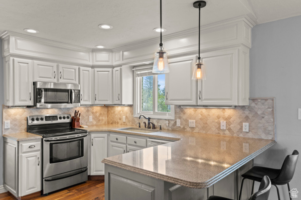 Kitchen featuring white cabinets, a breakfast bar, a sink, stainless steel appliances, and a peninsula