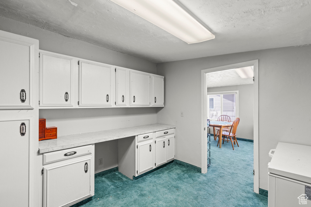 Carpeted home office with built in study area and a textured ceiling