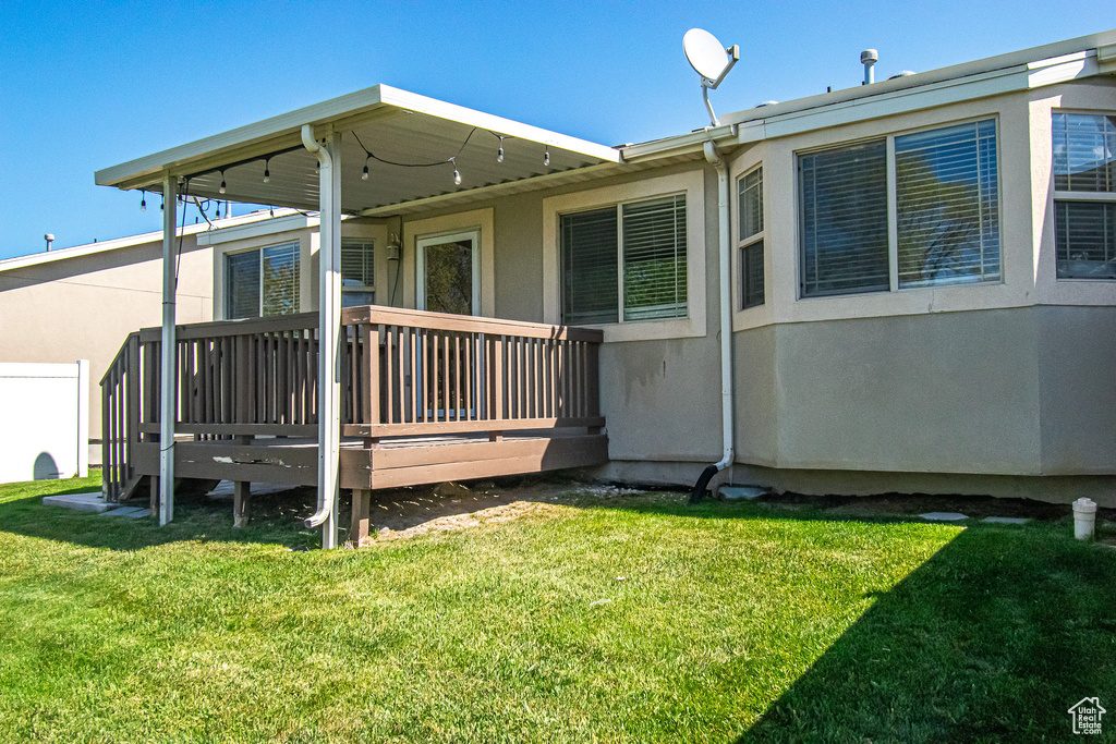 Rear view of house featuring a lawn, stucco siding, and a deck