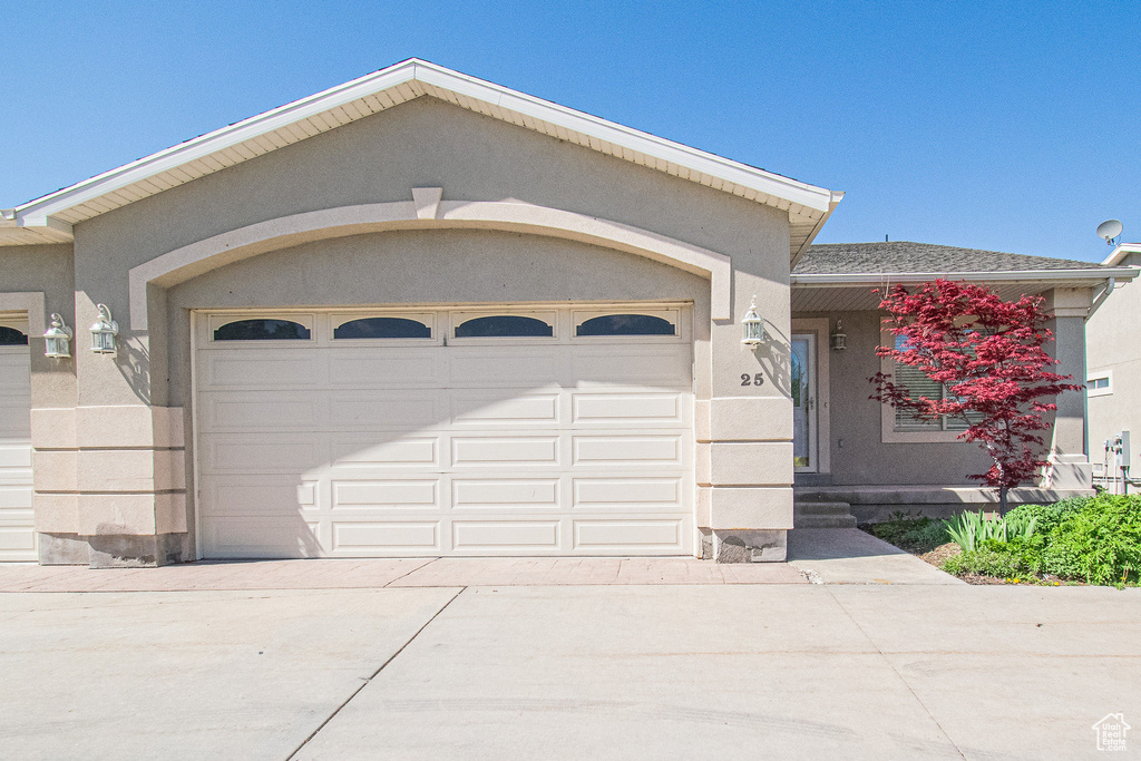 View of front of home featuring an attached garage, roof with shingles, stucco siding, and concrete driveway