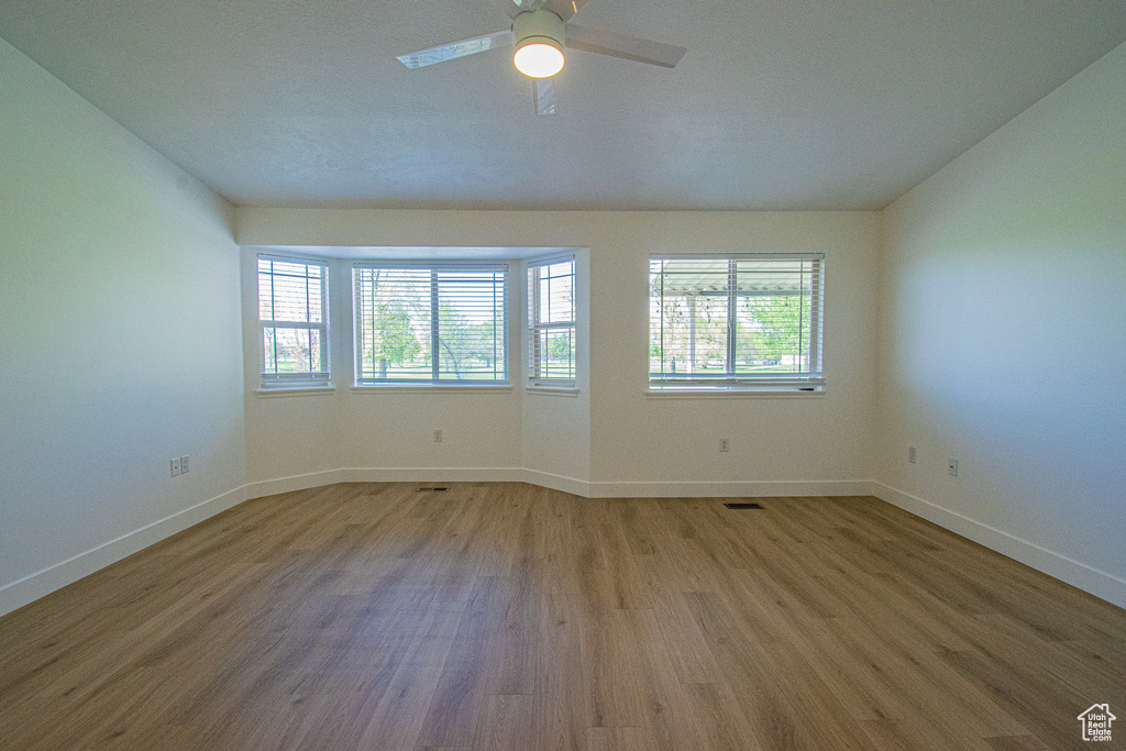 Spare room with a healthy amount of sunlight, baseboards, a ceiling fan, and wood finished floors
