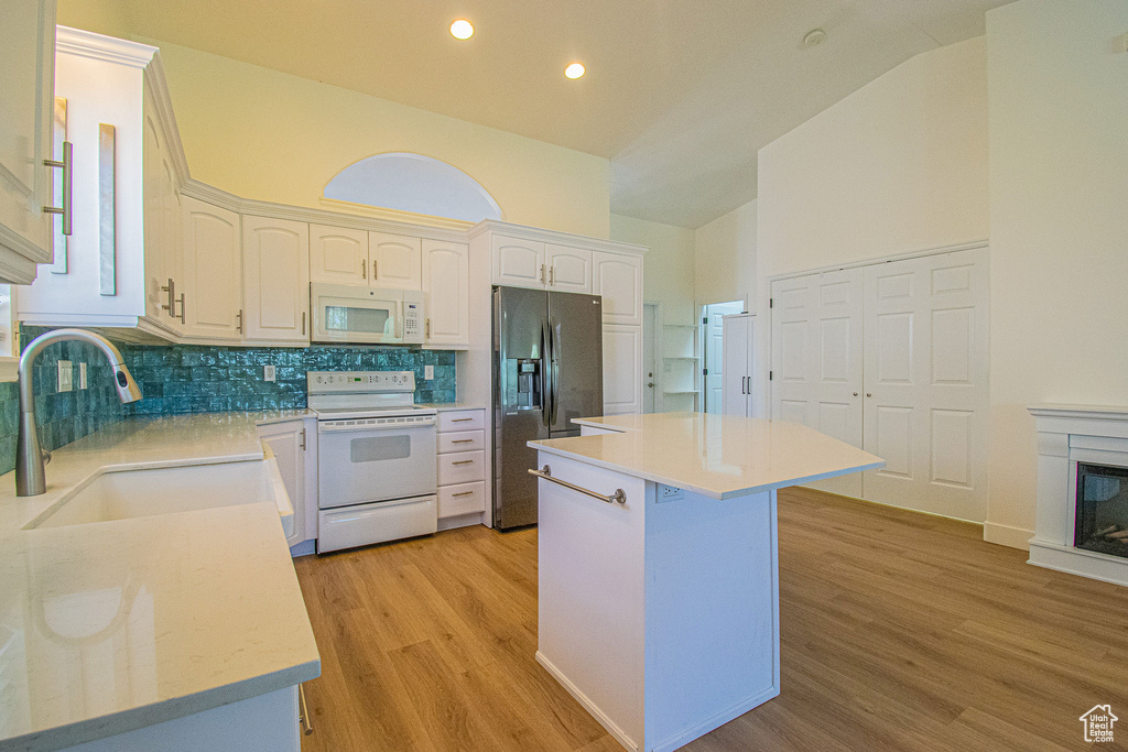 Kitchen featuring decorative backsplash, a sink, white cabinets, light wood-style floors, and white appliances