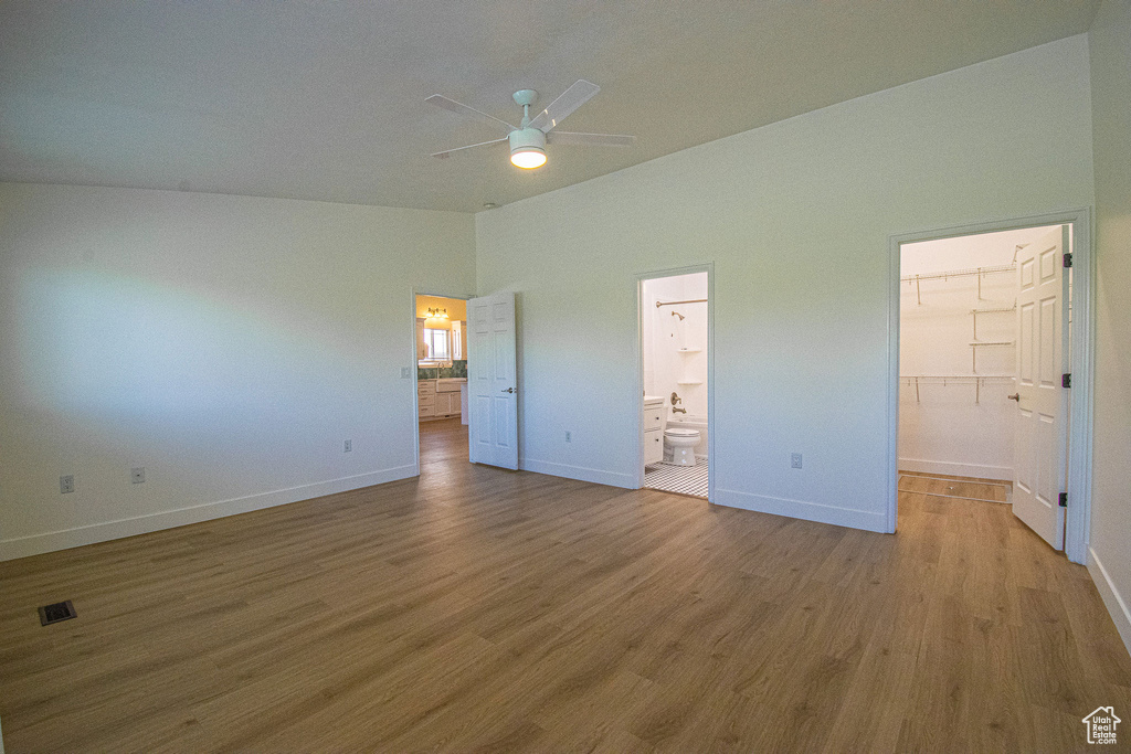 Unfurnished bedroom with baseboards, a walk in closet, lofted ceiling, and wood finished floors