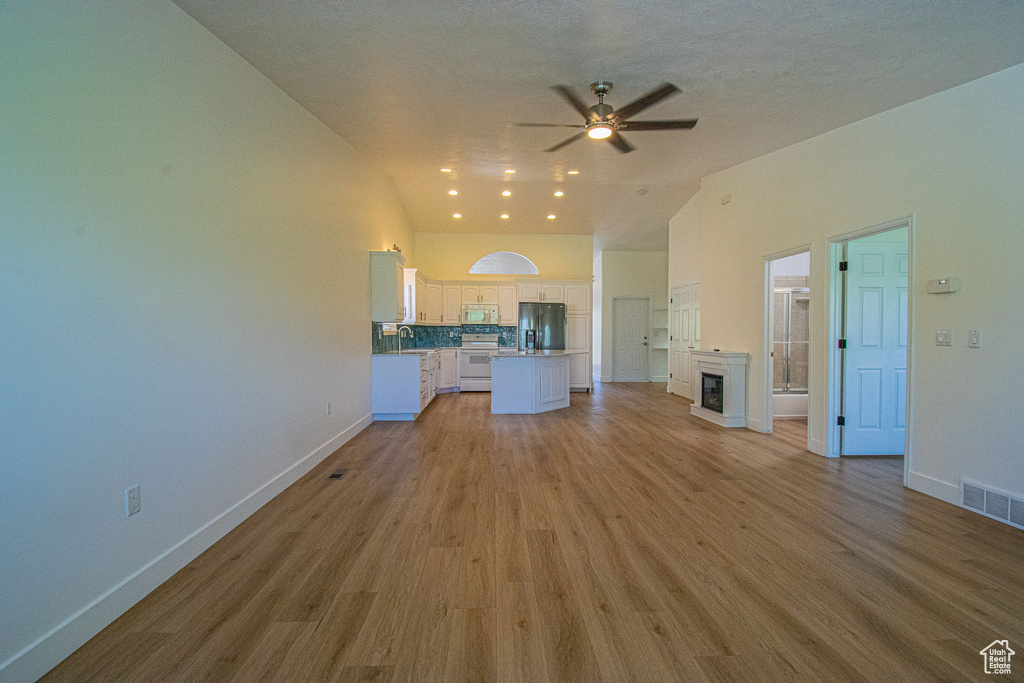 Unfurnished living room featuring baseboards, visible vents, ceiling fan, and lofted ceiling
