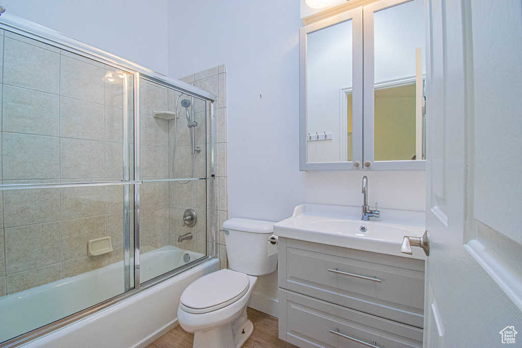 Full bathroom featuring vanity, bath / shower combo with glass door, wood finished floors, and toilet