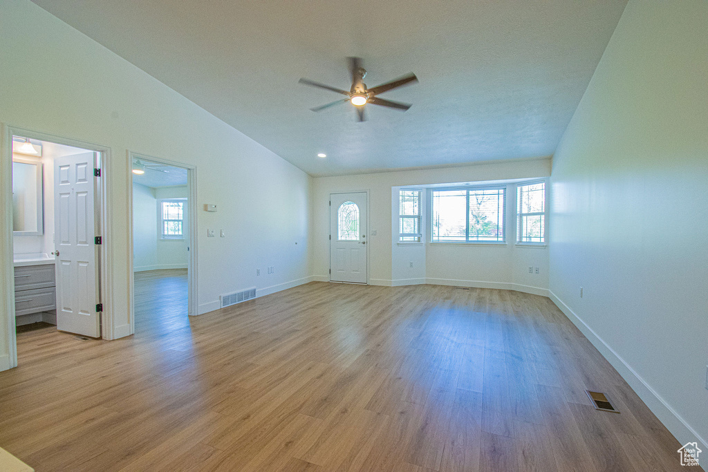 Empty room with light wood-style floors, ceiling fan, vaulted ceiling, and visible vents