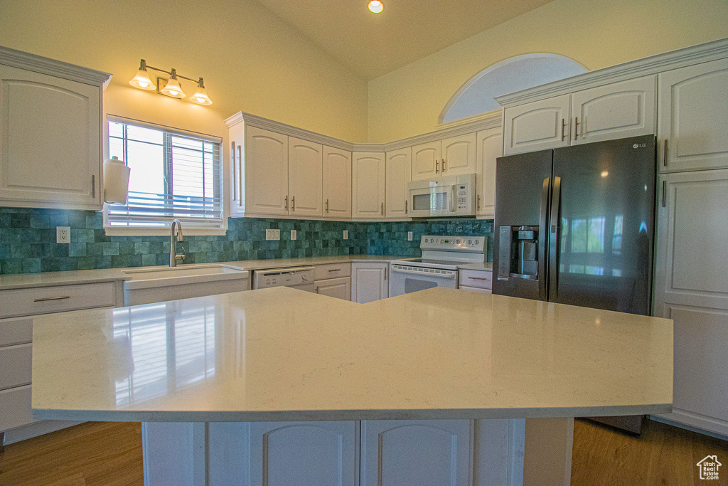Kitchen featuring backsplash, vaulted ceiling, a sink, light countertops, and white appliances
