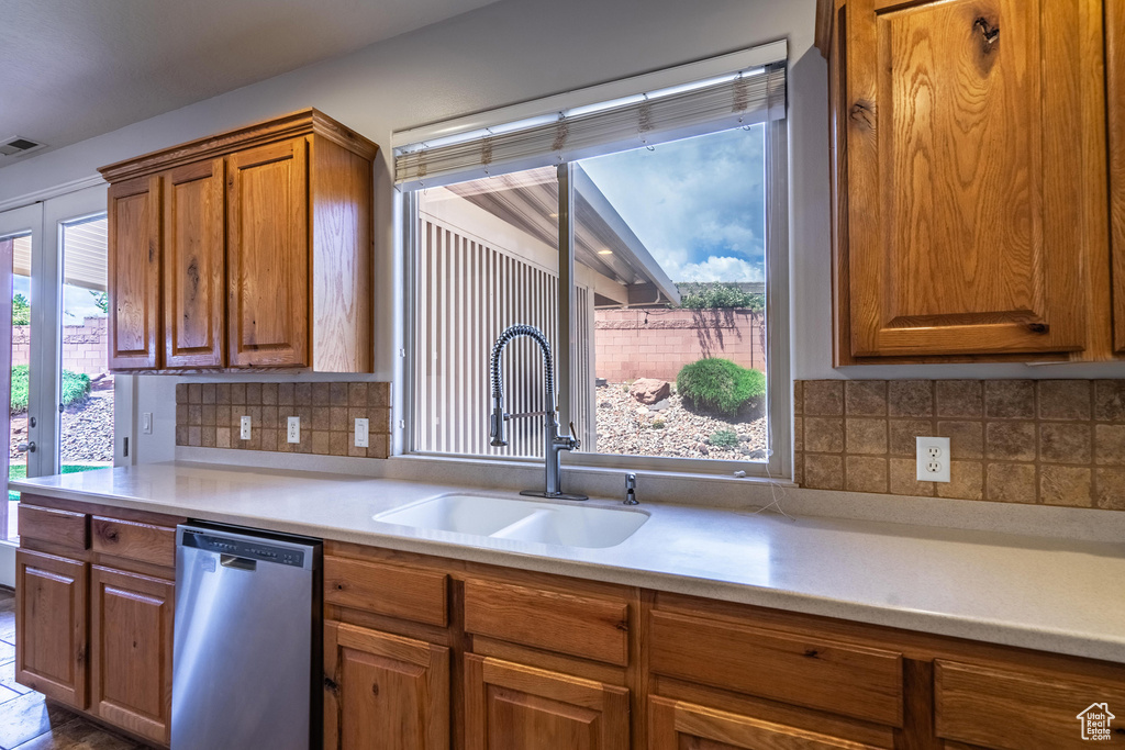 Kitchen featuring backsplash, brown cabinets, dishwasher, a sink, and light countertops