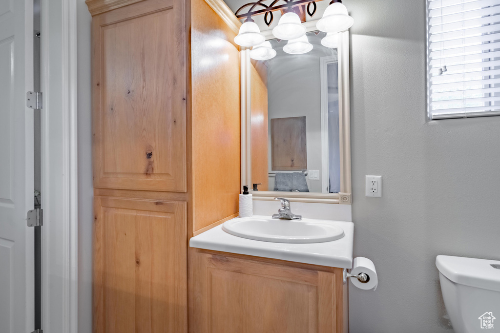 Half bath featuring an inviting chandelier, toilet, and vanity